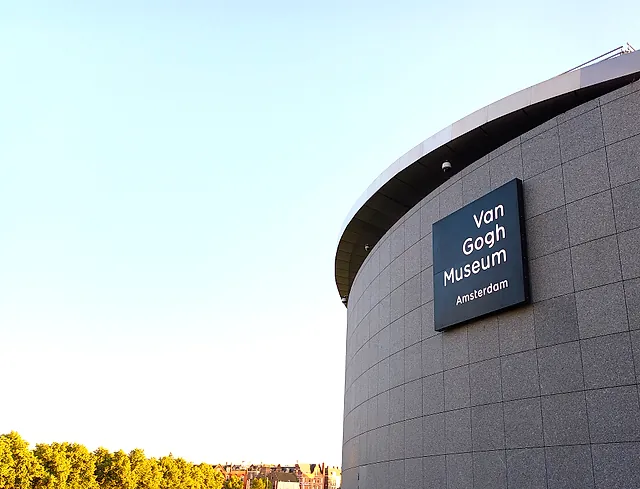 The curved grey-tiled wall of the Van Gogh Museum main building with its dark museum sign, under a clear blue sky